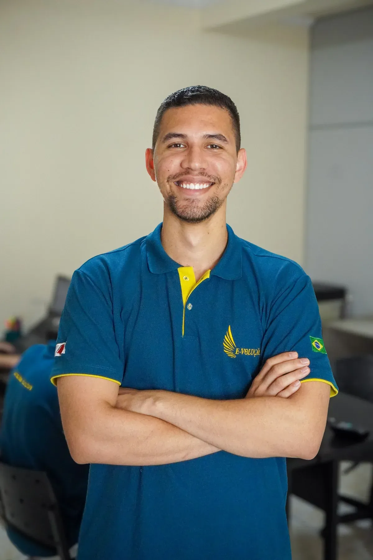 Integrante da equipe da E-volução sorrindo de braços cruzados no escritório